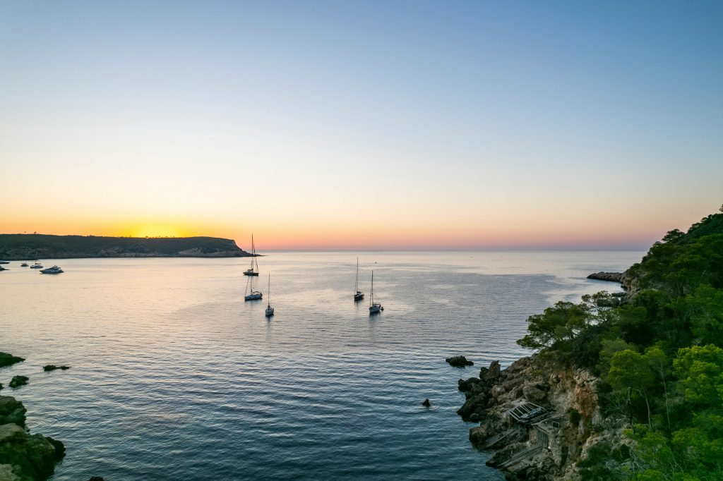 Sailing boats anchored in a peaceful bay during sunset in Sant Joan de Labritja, Spain.